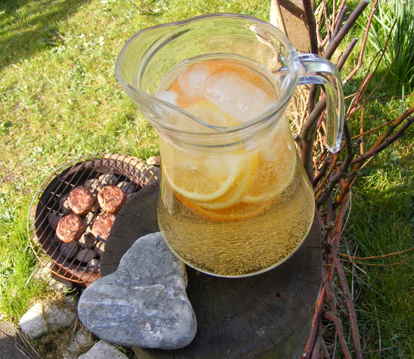 Image of ginger white wine spritzer next to a BBQ grill with beef burgers on it.
