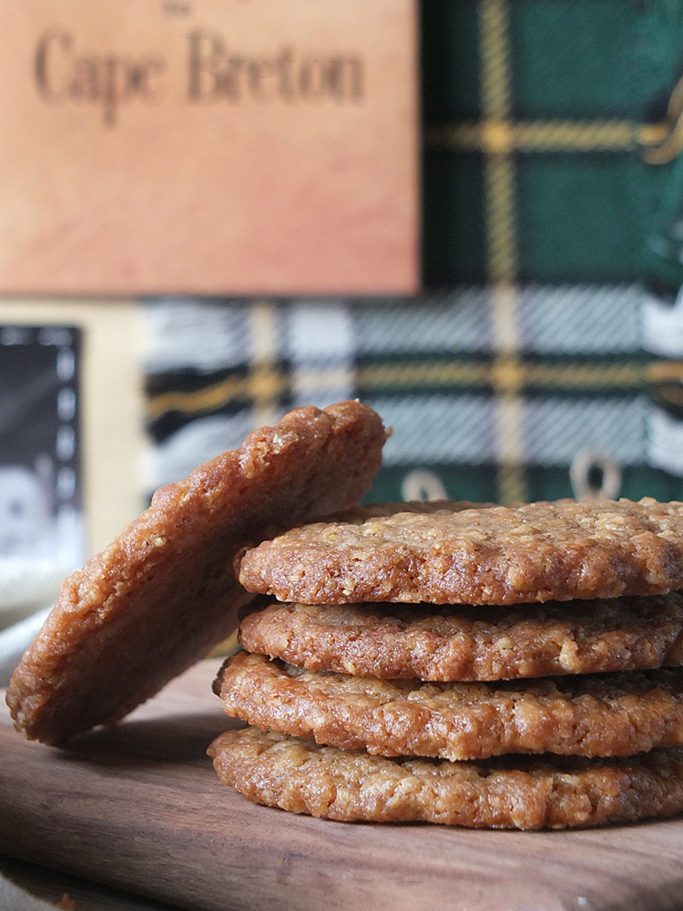 Close up image of a stack of buttery oatcakes with Cape Breton tartan blurred in the background.