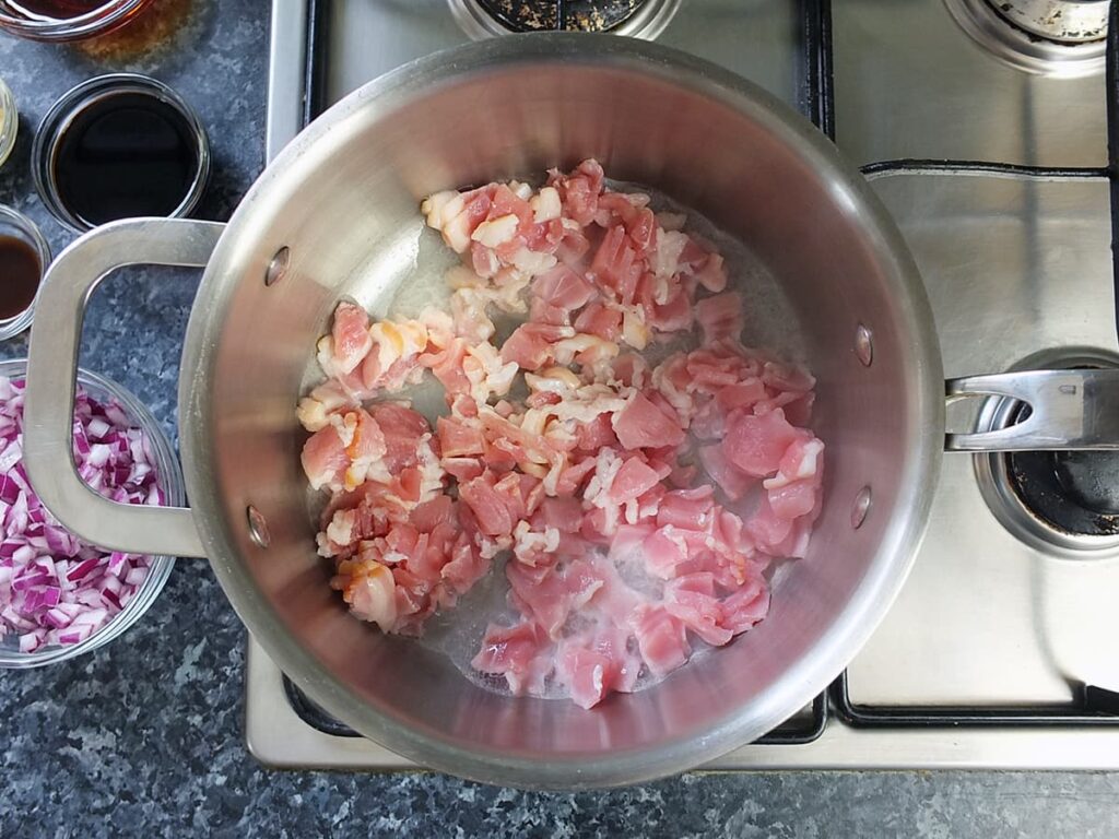 Image of bacon beginning to fry in a pan.