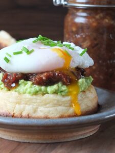 Photo of homemade bacon jam on a toasted, buttered crumpet with smashed avocado topped with a perfectly poached runny egg.