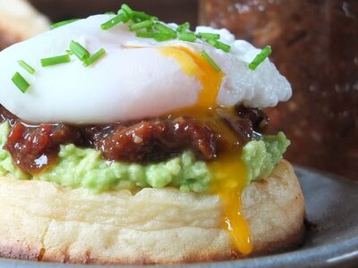 Photo of homemade bacon jam on a toasted, buttered crumpet with smashed avocado topped with a perfectly poached runny egg.