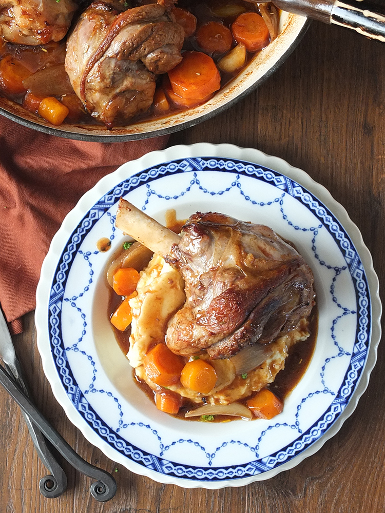 Top down photo of a slow cooked lamb shank on creamy mashed potatoes surrounded in vegetables and gravy.