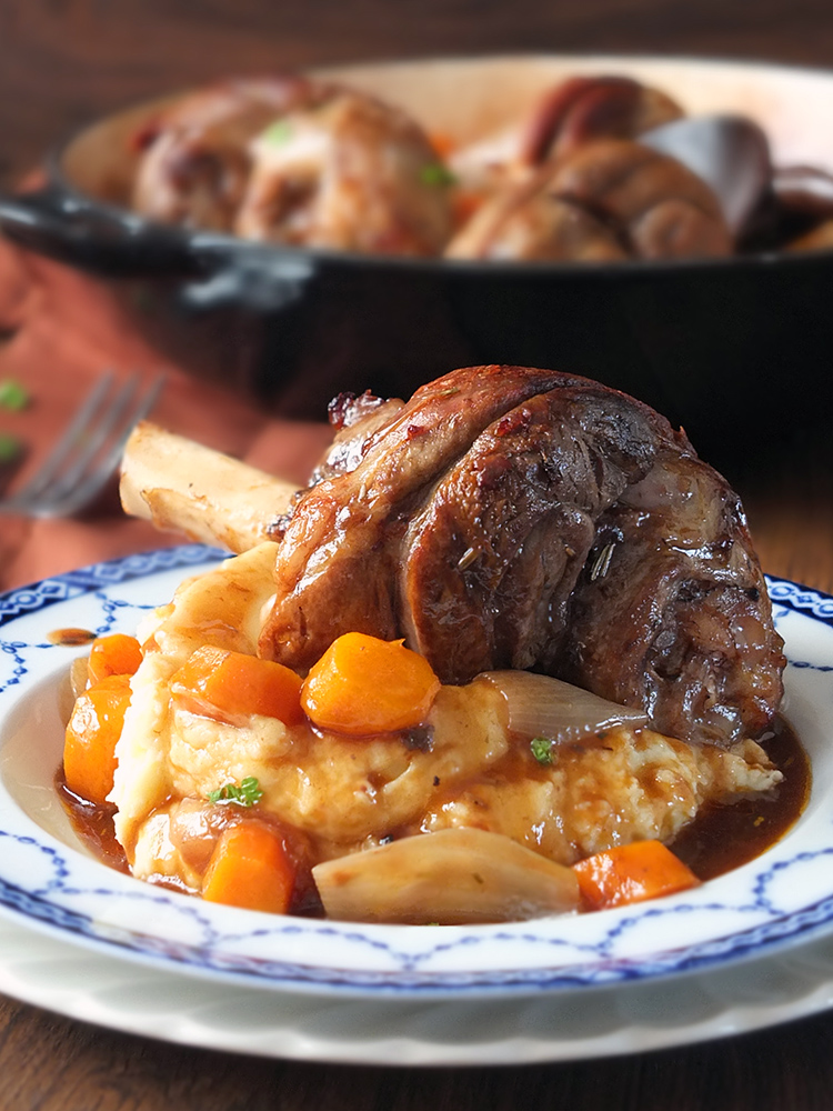 Image of a slow cooked lamb shank with vegetables and gravy on a bed of creamy mashed potatoes.