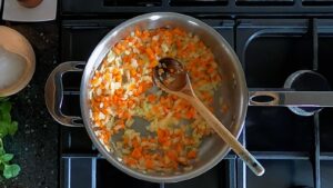 Image of saute pan with cooked garlic, carrot and onion in it.