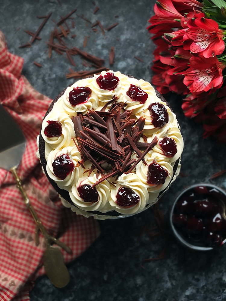 Layers of rich chocolate cake drizzled with cherry brandy sandwiched together with sweetened whipped cream and black cherry conserve. The cake is finished with more cream and some dark chocolate curls. #chocolate #chocolatecake #blackforestcake #baking