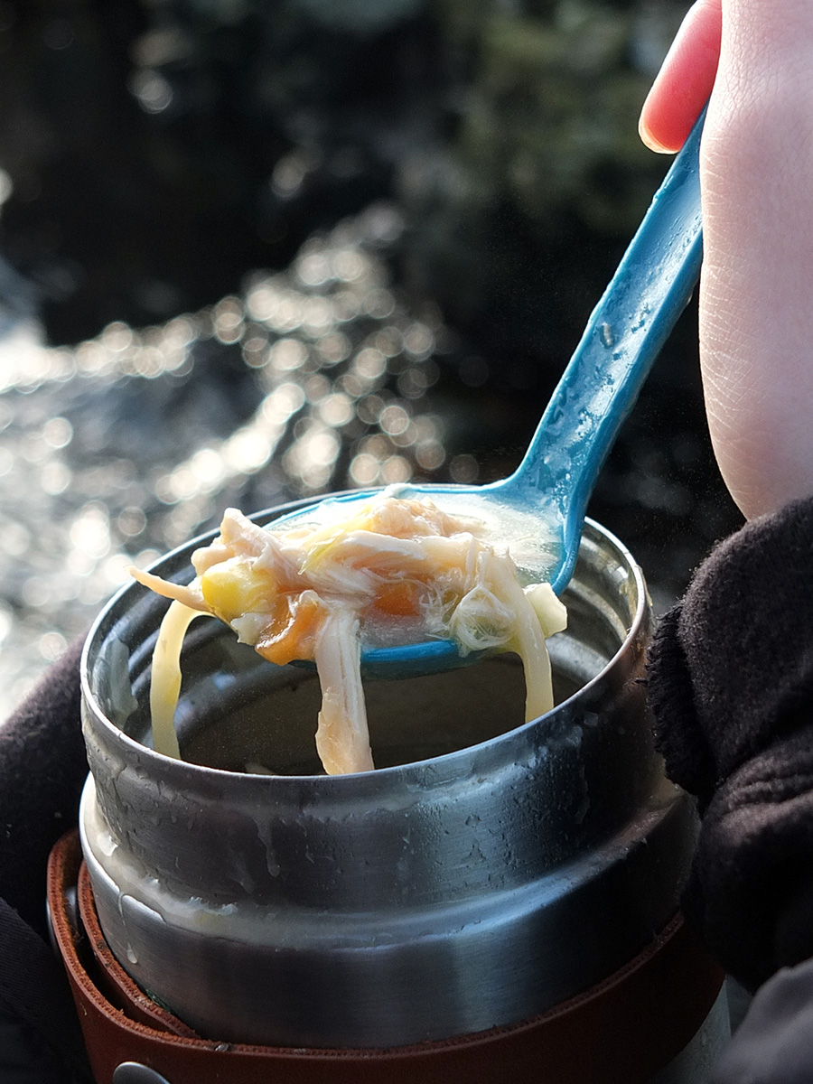 Close-up photo of a spoonful of chicken noodle Soup from a flask, outdoors.
