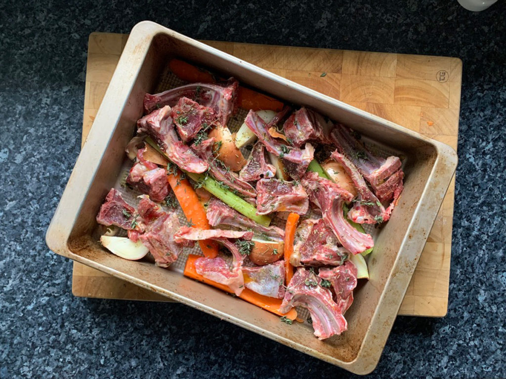 Top down photo of lamb bones and vegetables going to be made into lamb stock.