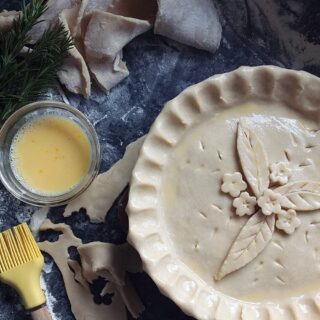 image of unbaked pie crust brushed with beaten egg and decorated with pastry leaves and flowers