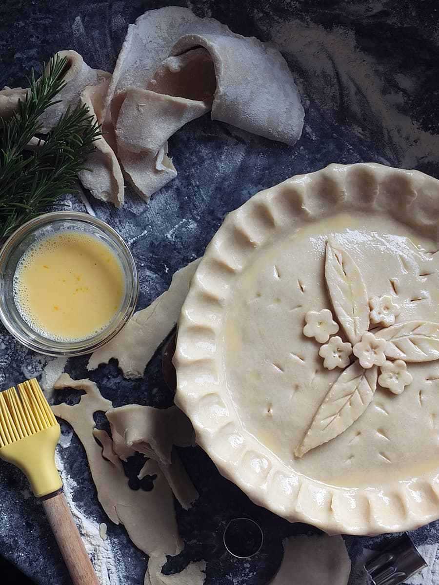 image of unbaked pie crust brushed with beaten egg and decorated with pastry leaves and flowers