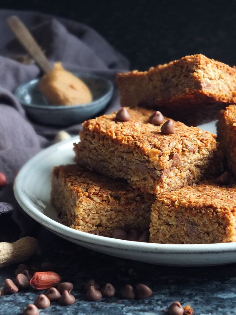 Image of peanut butter flapjacks on a plate with chocolate chips sprinkled on top and a spoonful of peanut butter in the background.