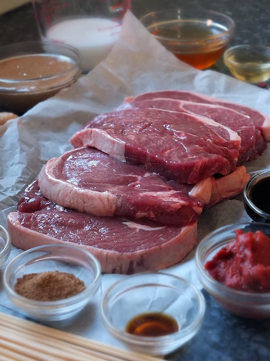 Close up photo of raw lamb leg steaks and ingredients for this recipe for lamb skewers.