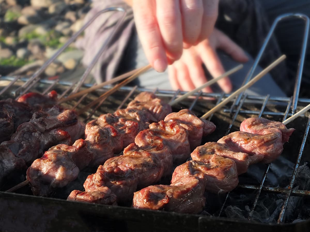 Image of a recipe for lamb skewers cooking on a beach barbecue.