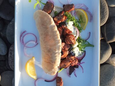 photograph of bbq lamb shoulder and tzatziki pittas on an enamel tray on a rocky beach in Shetland