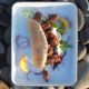 photograph of bbq lamb shoulder and tzatziki pittas on an enamel tray on a rocky beach in Shetland