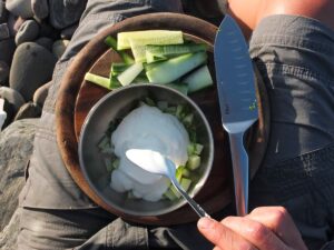 Image of man spooning yogurt into bowl of cucumber and mint to make tzatziki.