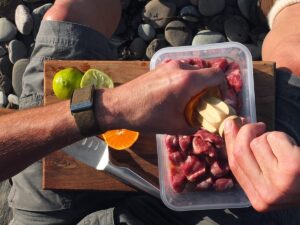 Photograph of man's hands squeezing orange juice over lamb to marinade it.