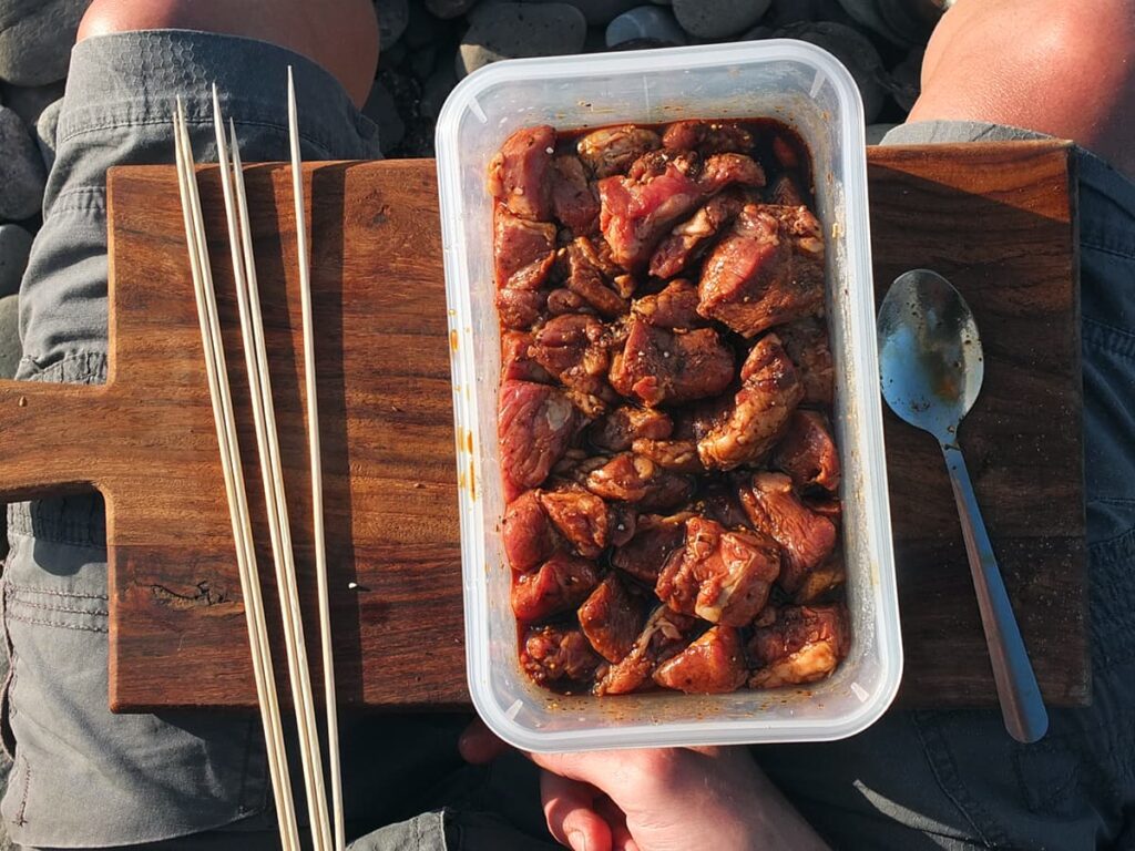 Image of lamb marinading in plastic container on the beach.