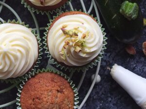 Photo of spiced courgette cupcakes being frosted with cream cheese frosting and decorated with chopped pistachios.