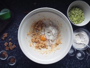 Top down image of mixing bowl with a cracked egg in the creamed butter and sugars and a spoonful of flour.