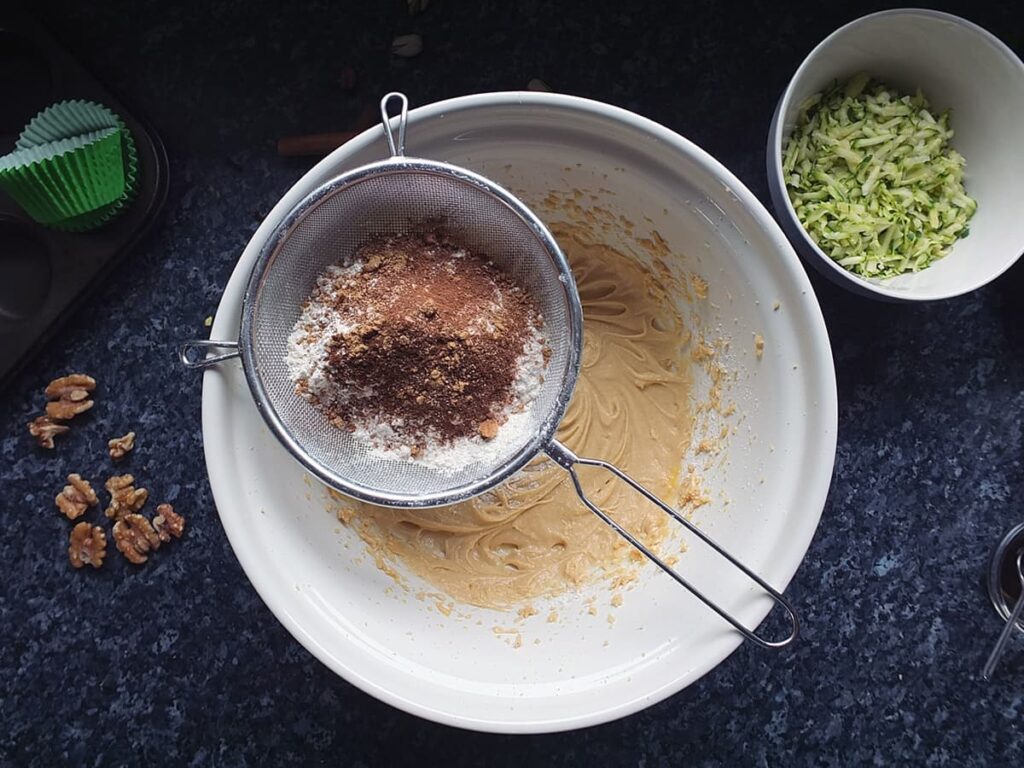Image of mixing bowl with a sieve of dry ingredients over the top.