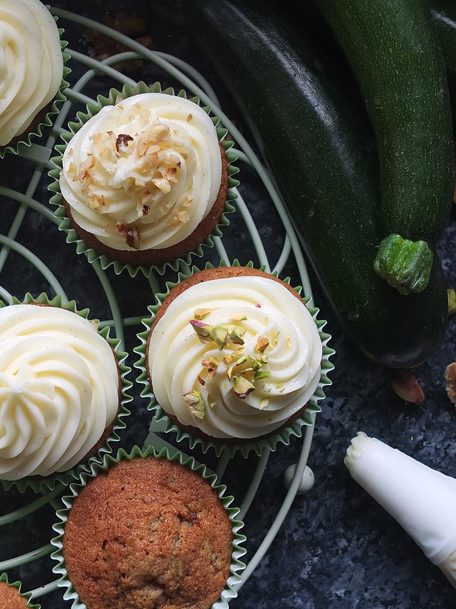 Top down image of zucchini cupcakes with a swirl of cream cheese frosting topped with chopped nuts. 