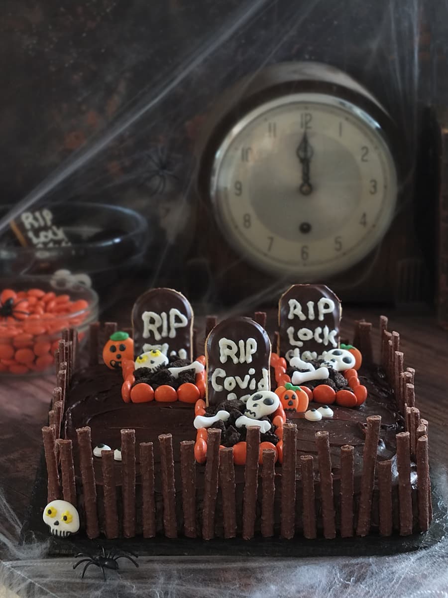 Image of a chocolate Halloween graveyard cake with three spooky graves surrounded by a chocolate matchmakers crooked fence.
