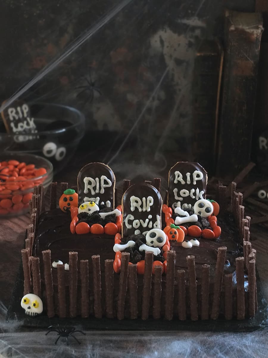 Image of a chocolate Halloween graveyard cake with three spooky graves surrounded by a chocolate matchmakers crooked fence.