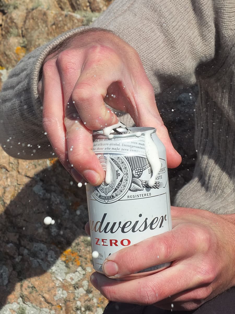 Image of man's hand opening tin of zero alcohol beer with beer foam spraying out of the tin.