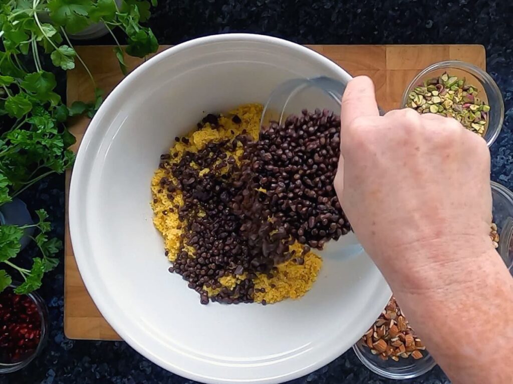 Image of a bowl of puy lentils being poured into a bowl of couscous.