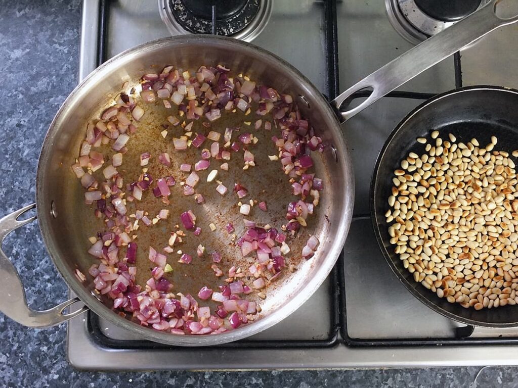 Image of sauteed red onions in a pan and toasted pine nuts in a second pan.