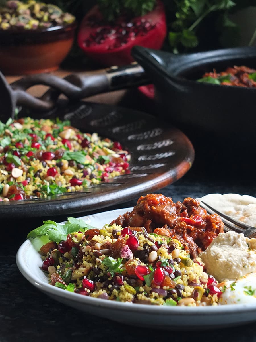 Image of jewelled couscous recipe on a serving plate with Moroccan-style slow cooked lamb, hummus, flatbread and plain yoghurt.