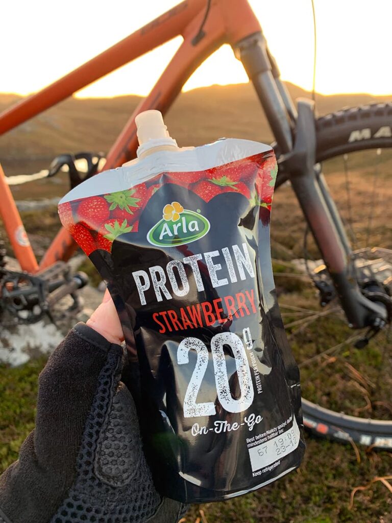 Image of Arla Protein 20 pouch with a muddy mountainbike in the background.