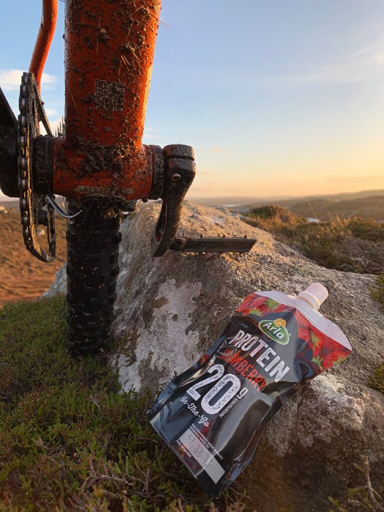 Image of Arla Protein 20 pouch with a muddy mountainbike in the background.