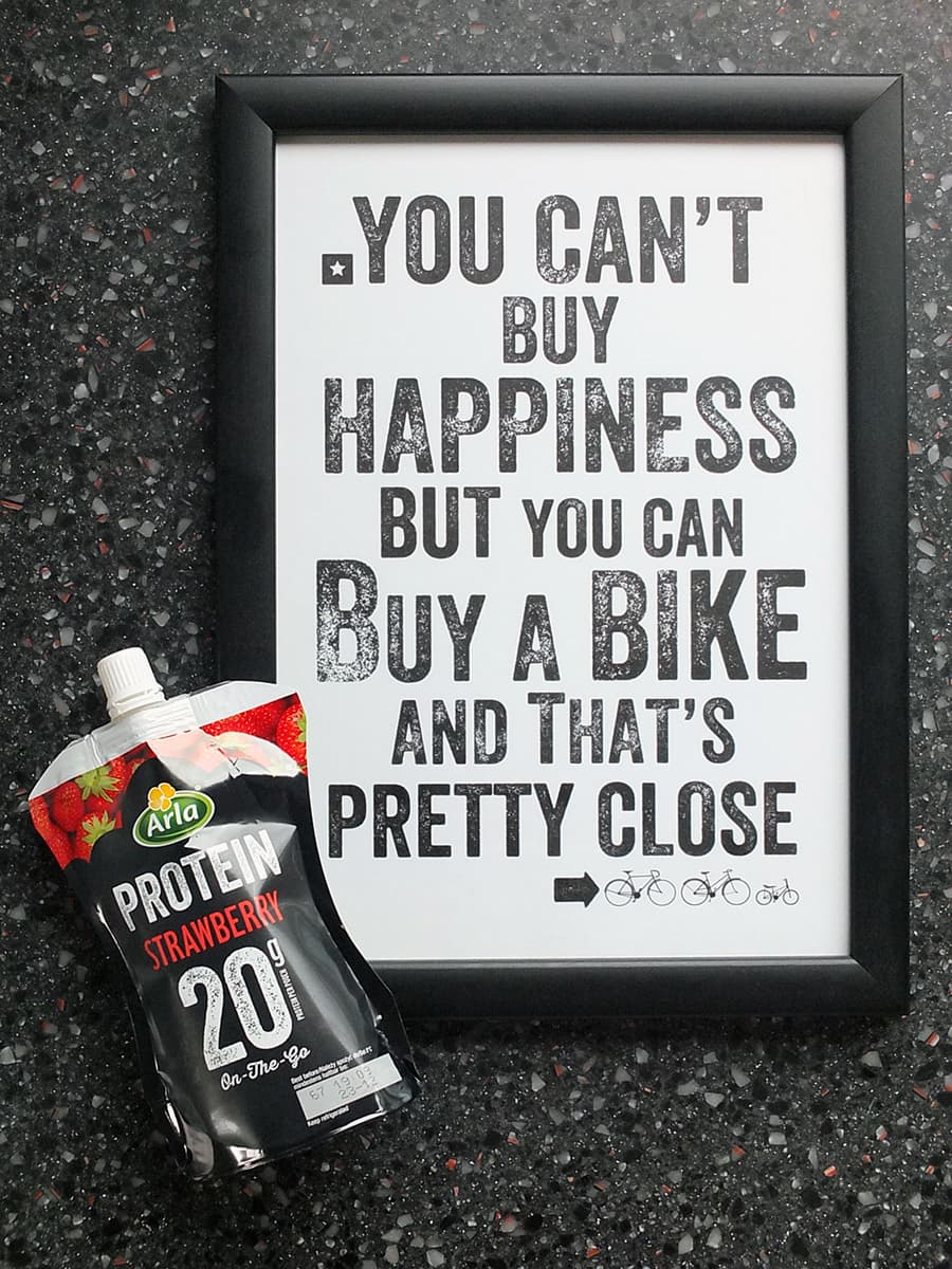 Image of a framed print with the words: you can't buy happiness but you can buy a bike and that's pretty close' with the Arla Protein 20 pouch in the bottom left hand corner.