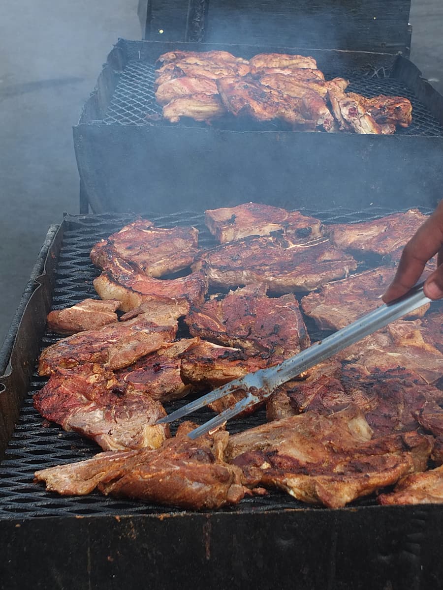 Image of half of a black oil drum turned into a BBQ with pork and chicken cooking on it.