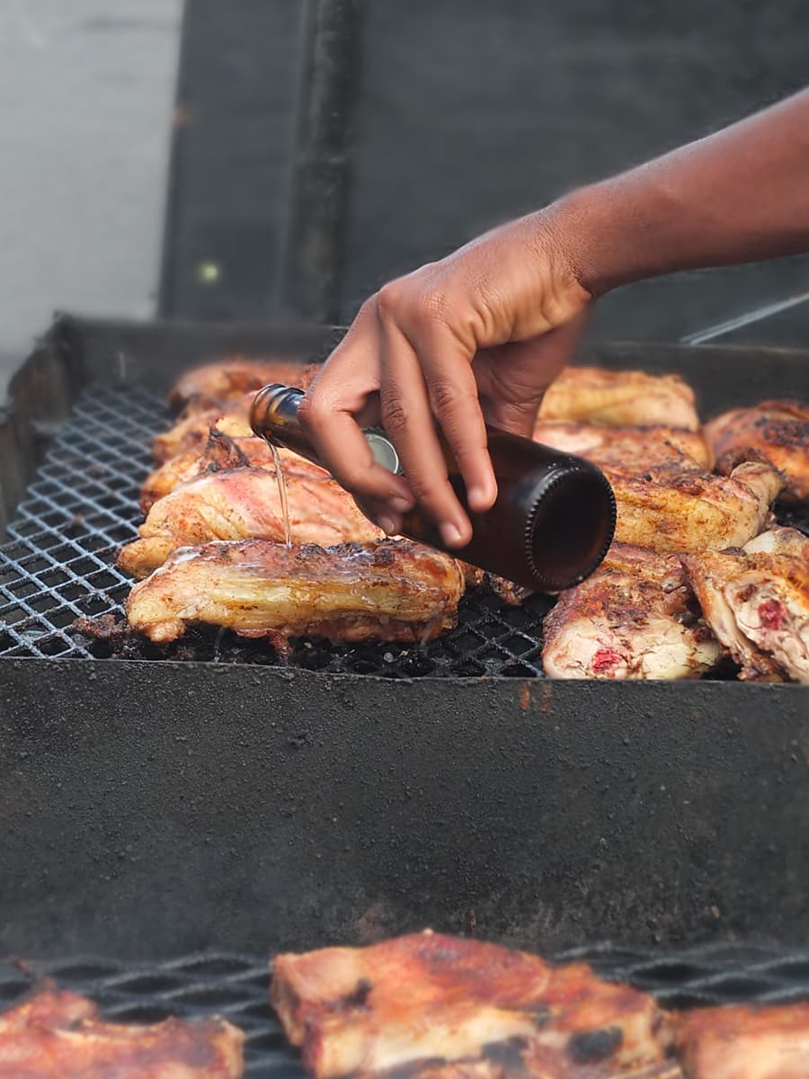 Image of man pouring beer over barbecuing chicken.