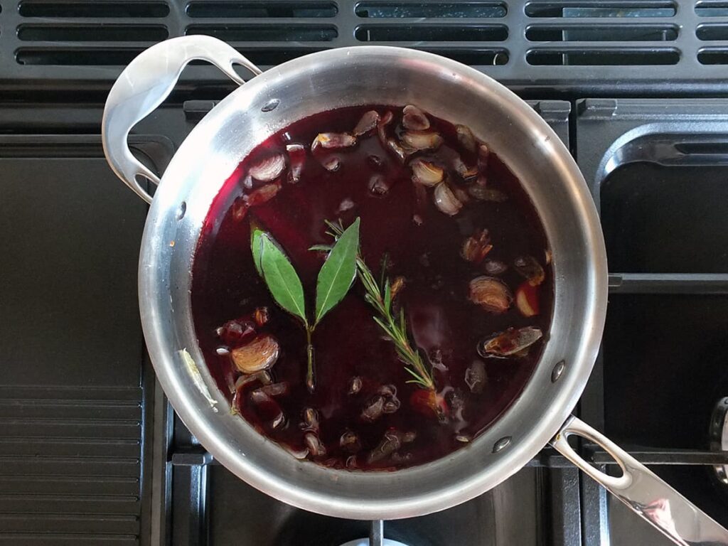 Top down image of port, red wine and herbs in saute pan.