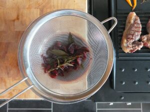Top down image of red wine jus being strained through a fine mesh strainer.