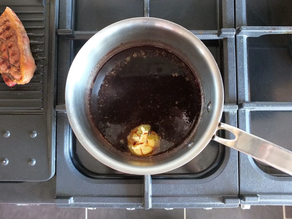 Top down image of red wine jus in pan with butter melting in it.