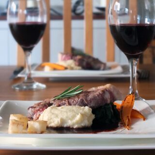 Image of lamb leg steak being served on a white plate with celeriac puree and red wine jus.