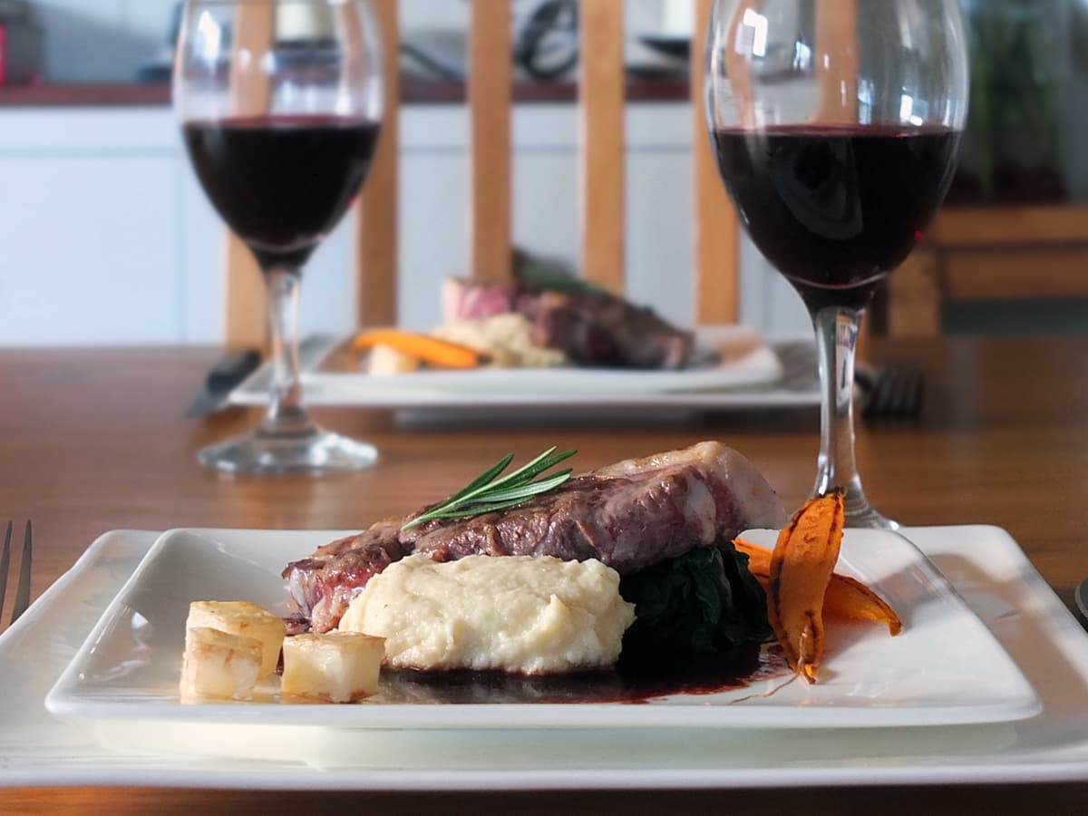 Image of lamb leg steak being served on a white plate with celeriac puree and red wine jus.