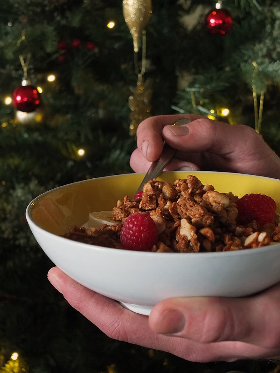 Image of man's hands holding a bowl of peanut butter granola. There's a little bit of oil on his fingers as he's a cyclist and he had a tyre puncture just before I asked him to be my hand model. 