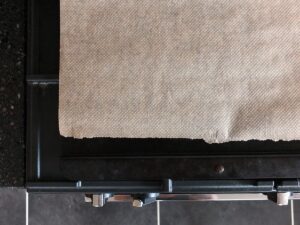 Top down image of a Netherton Foundry wrought iron baking tray on top of a rangemaster oven with a piece of baking paper on it.