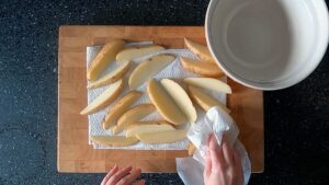 Image of hands patting potato wedges dry with paper towel.