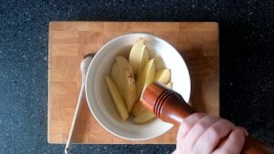 Image of hands seasoning potato wedges with a handcarved wooden pepper mill (it's a beautiful pepper mill made by my partner's father).