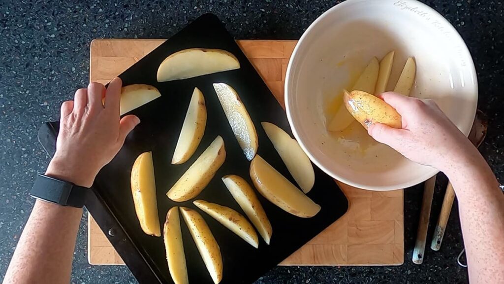 Image of hands arranging seasoned potato wedges on a wrought iron baking tray.