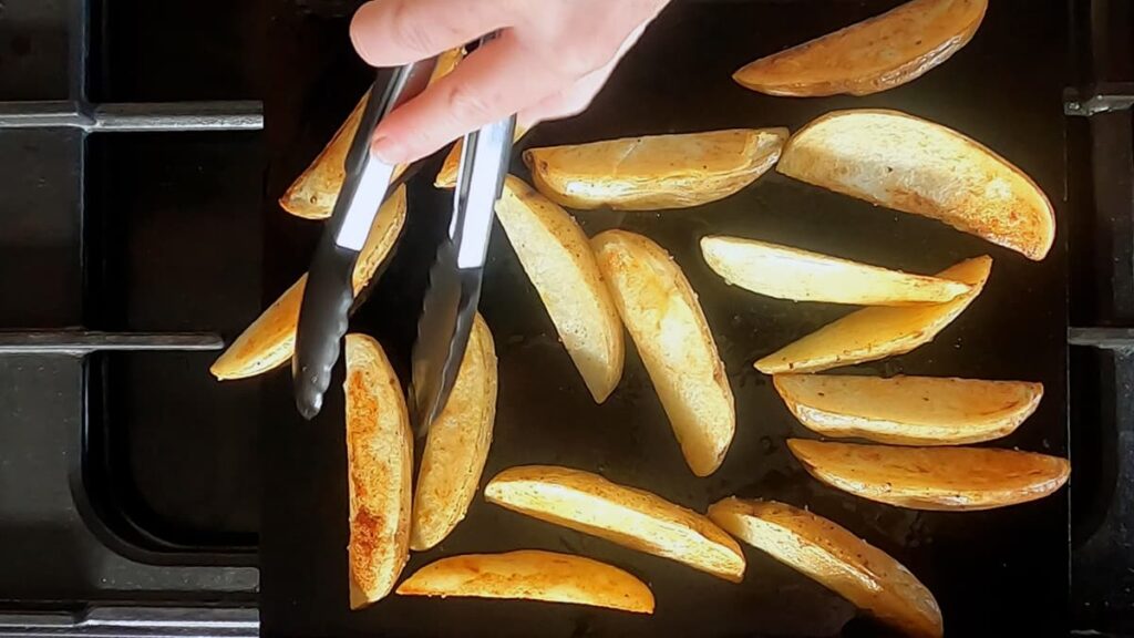 Image of hand with tongs turning browned potato wedges over.