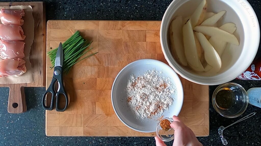 Image of hand sprinkling Cajun spice over a plate of flour.