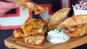 Image of man's hands holding gastro platter of food, poised to dip potato wedge into blue cheese dip.