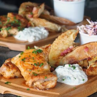 Spicy honey glazed chicken thighs on a wooden gastro pub board with cheesy bacon potato wedges, blue cheese dip and coleslaw.